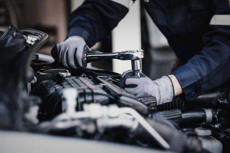 Mechaniker mit Handschuhen bei Reparaturarbeiten am Motor